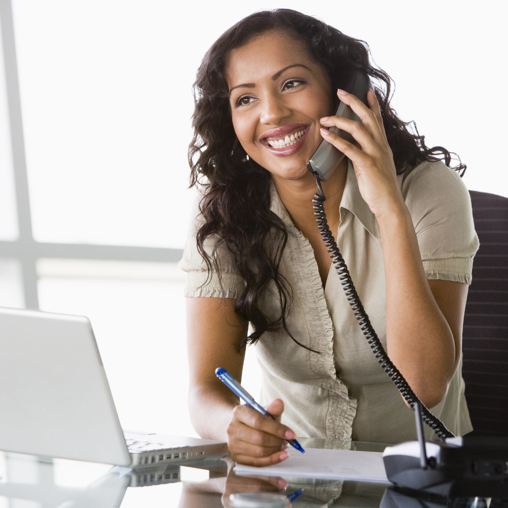 Woman on the phone at a desk with a laptop and pen
